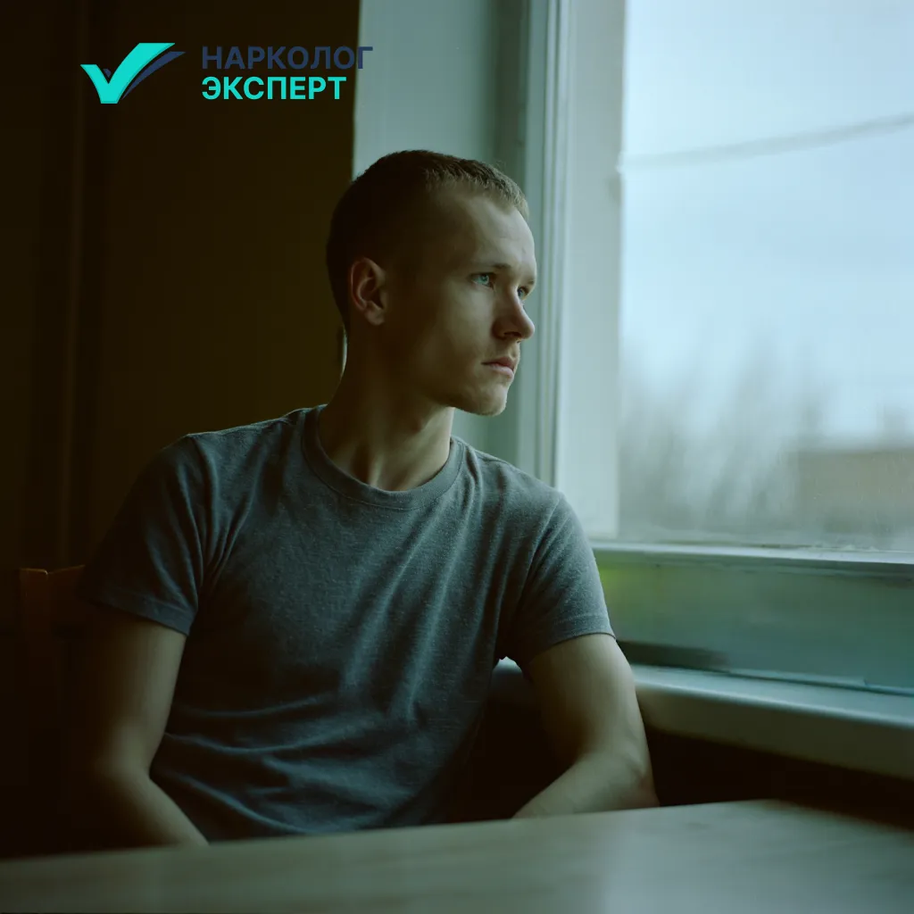 Молодой парень в депрессивном состоянии сидит за столом и смотрит в окно